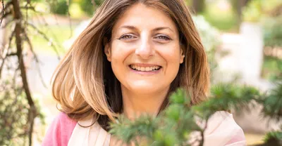 Portrait de Gabrielle Ladevant, professeure de yoga, souriante parmi les branches d'un arbre ensoleillé