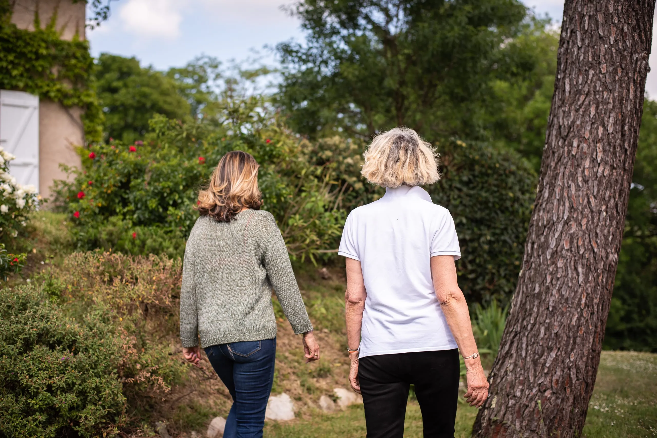 Deux femmes marchant côte à côte dans un jardin verdoyant, illustrant l'accompagnement bienveillant proposé par Gabrielle Ladevant.