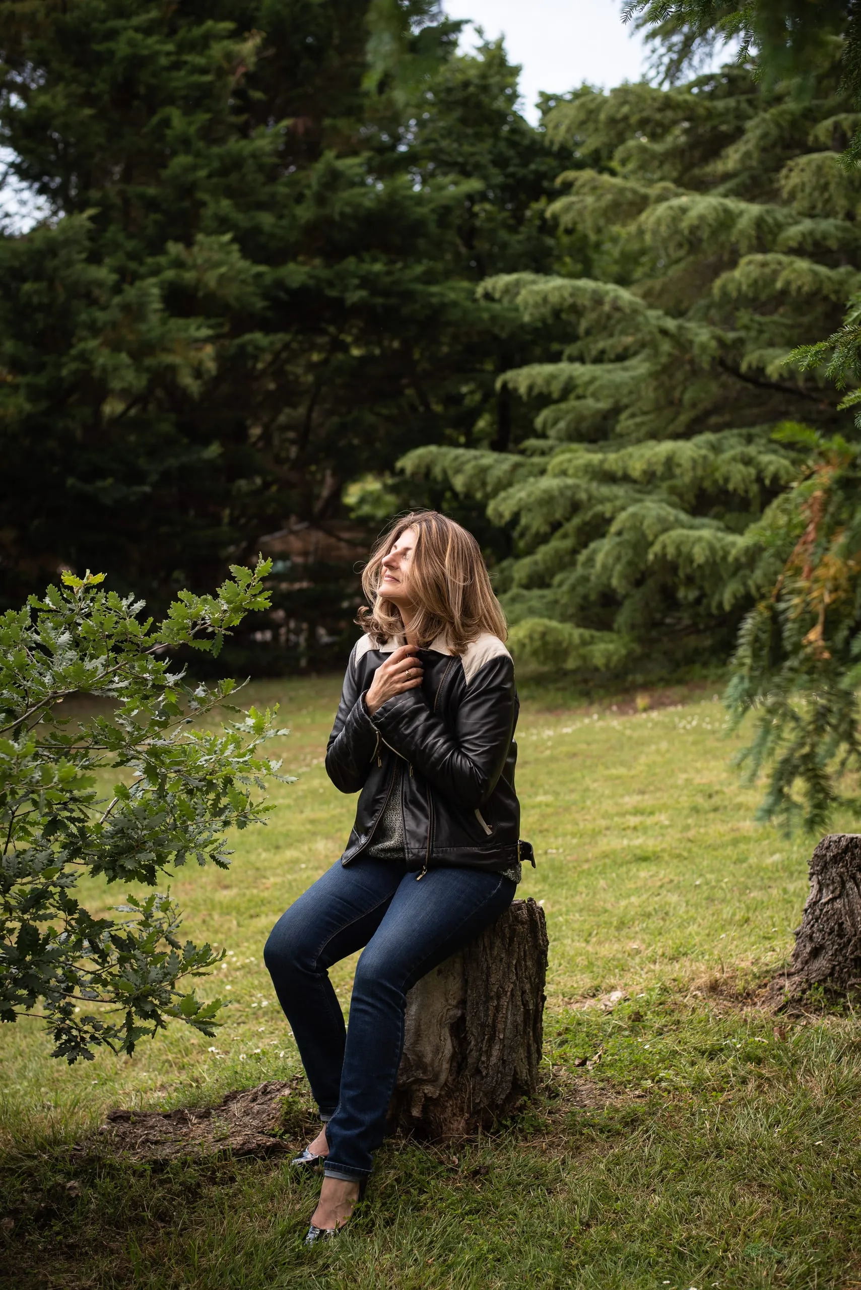 Gabrielle Ladevant, coach et professeure de yoga, assise sur un tronc d'arbre dans la nature, les mains sur le coeur, regard vers le ciel.