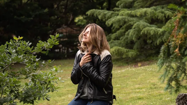 Gabrielle Ladevant, coach et professeure de yoga, assise sur un tronc d'arbre dans la nature, les mains sur le coeur, regard vers le ciel.