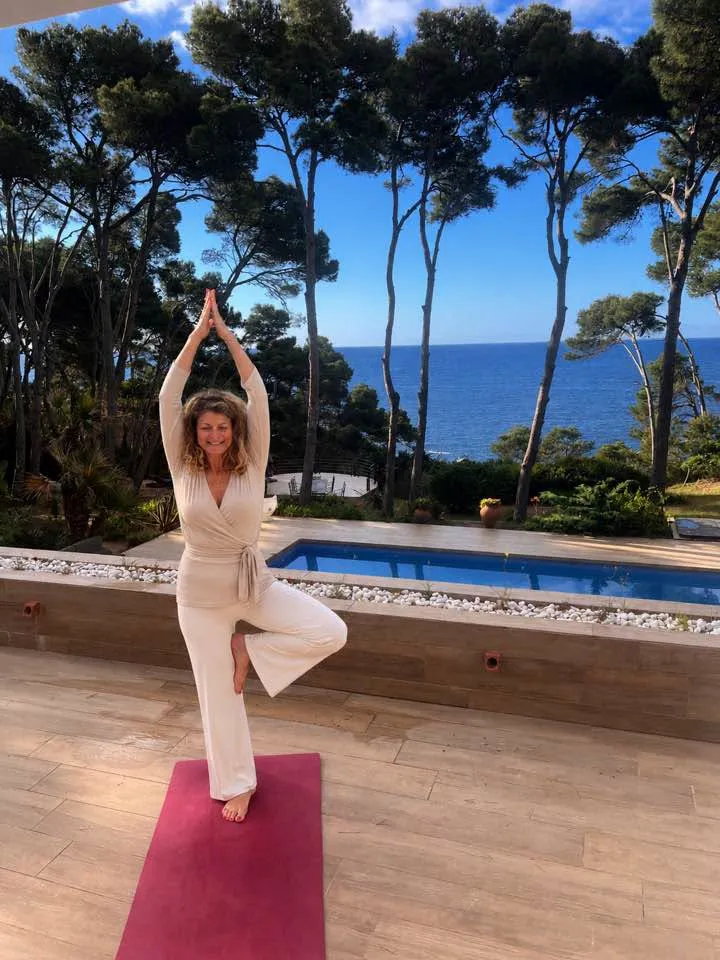Gabrielle en posture de l’arbre sur un tapis rose, devant une piscine et la mer